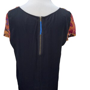 May include: Black short-sleeved top with a back zipper and floral print on the sleeves. The floral print is in shades of orange, red, and purple.