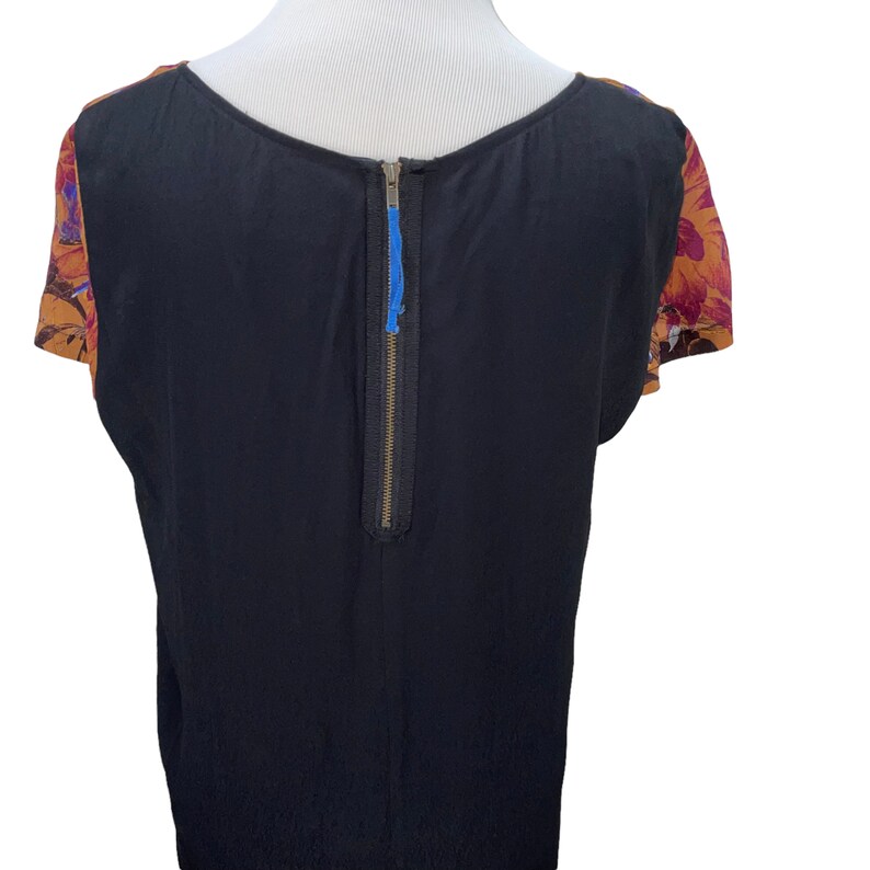 May include: Black short-sleeved top with a back zipper and floral print on the sleeves. The floral print is in shades of orange, red, and purple.
