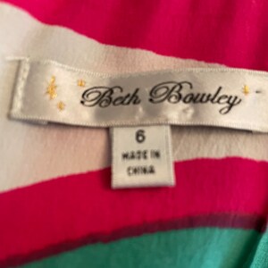 Peut inclure: Tissu ray&eacute; blanc et rose avec une bande verte en bas. Une &eacute;tiquette blanche avec le texte "Beth Bowley" et une plus petite &eacute;tiquette blanche avec le texte "6" et "Fabriqu&eacute; en Chine" est attach&eacute;e.
