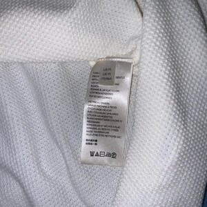 May include: Close-up of a white textured fabric with a tag attached. The tag includes washing instructions and size information. The fabric has a subtle, grid-like pattern, and the tag indicates a gentle wash cycle.