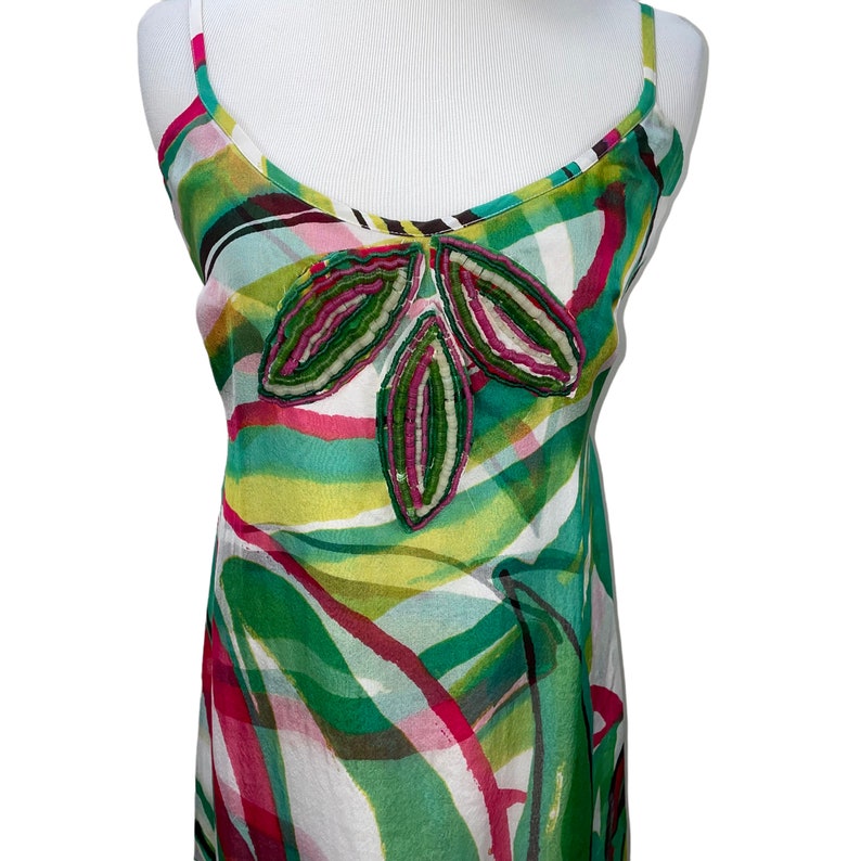 Peut inclure: Une robe blanche sans manches avec un imprim&eacute; abstrait vert, rose et jaune. La robe a un motif floral perl&eacute; sur le devant.