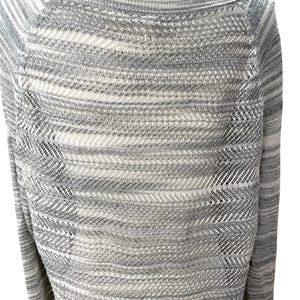 Puede incluir: Un su&eacute;ter a rayas grises y blancas con cuello barco. El su&eacute;ter tiene un dise&ntilde;o de punto texturizado con detalles calados en los laterales. Las mangas son largas y el estilo general es informal.