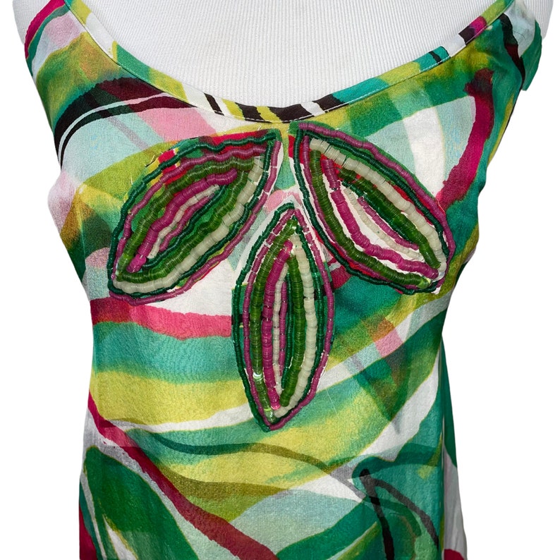 Peut inclure: Un haut blanc sans manches avec un imprim&eacute; abstrait vert, rose et jaune. Le haut pr&eacute;sente un motif de perles en forme de trois feuilles.