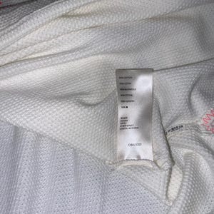 May include: Close-up of a white textured fabric with a label attached. The fabric has a waffle-like pattern. The label includes text in multiple languages, including English, and a barcode.