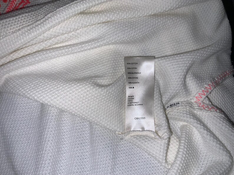 May include: Close-up of a white textured fabric with a label attached. The fabric has a waffle-like pattern. The label includes text in multiple languages, including English, and a barcode.