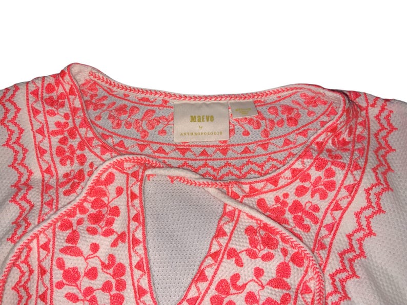 May include: White top with coral embroidery. The embroidery features floral and geometric patterns around the neckline and along the edges. The tag reads "Marvo by Anthropologie".