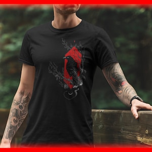May include: Black t-shirt with a graphic of a crow perched on a branch in a red diamond shape.