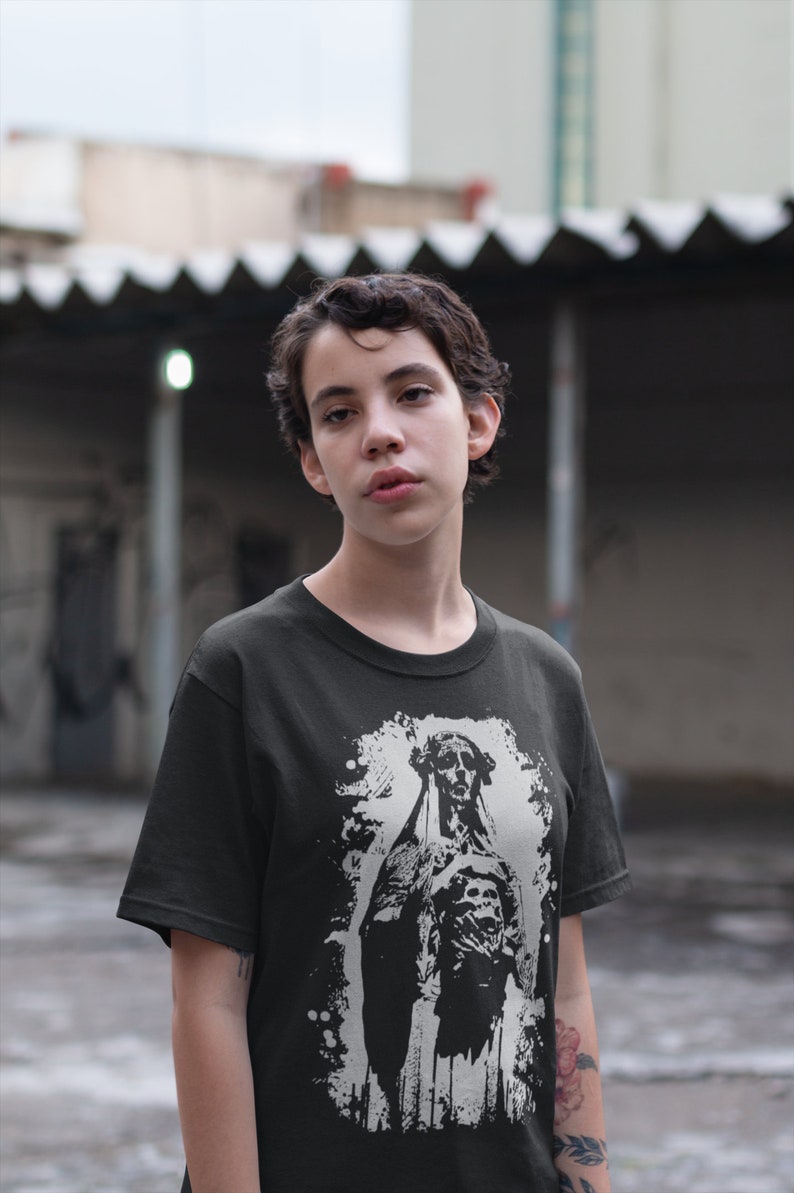 May include: A black t-shirt with a white graphic print of a skeletal figure in a hooded robe. The figure is standing with its arms crossed and has a distressed, grunge-style background.