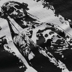 May include: Black and white graphic print of a skull with a bandana on a black t-shirt. The skull is wearing a bandana and has a distressed look.