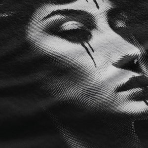 May include: Close-up of a black and white halftone image of a woman's face. The image is printed on a black fabric.