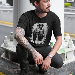 May include: A black t-shirt with a graphic print of a skeleton wearing a hat and holding a skull. The skeleton is in a distressed, faded, and white color.