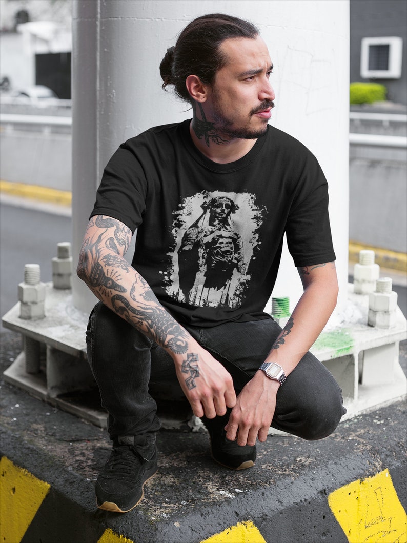 May include: A black t-shirt with a graphic print of a skeleton wearing a hat and holding a skull. The skeleton is in a distressed, faded, and white color.
