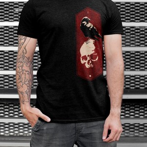 May include: A black t-shirt with a red graphic of a crow perched on a skull. The graphic is in a vintage style with a distressed look.