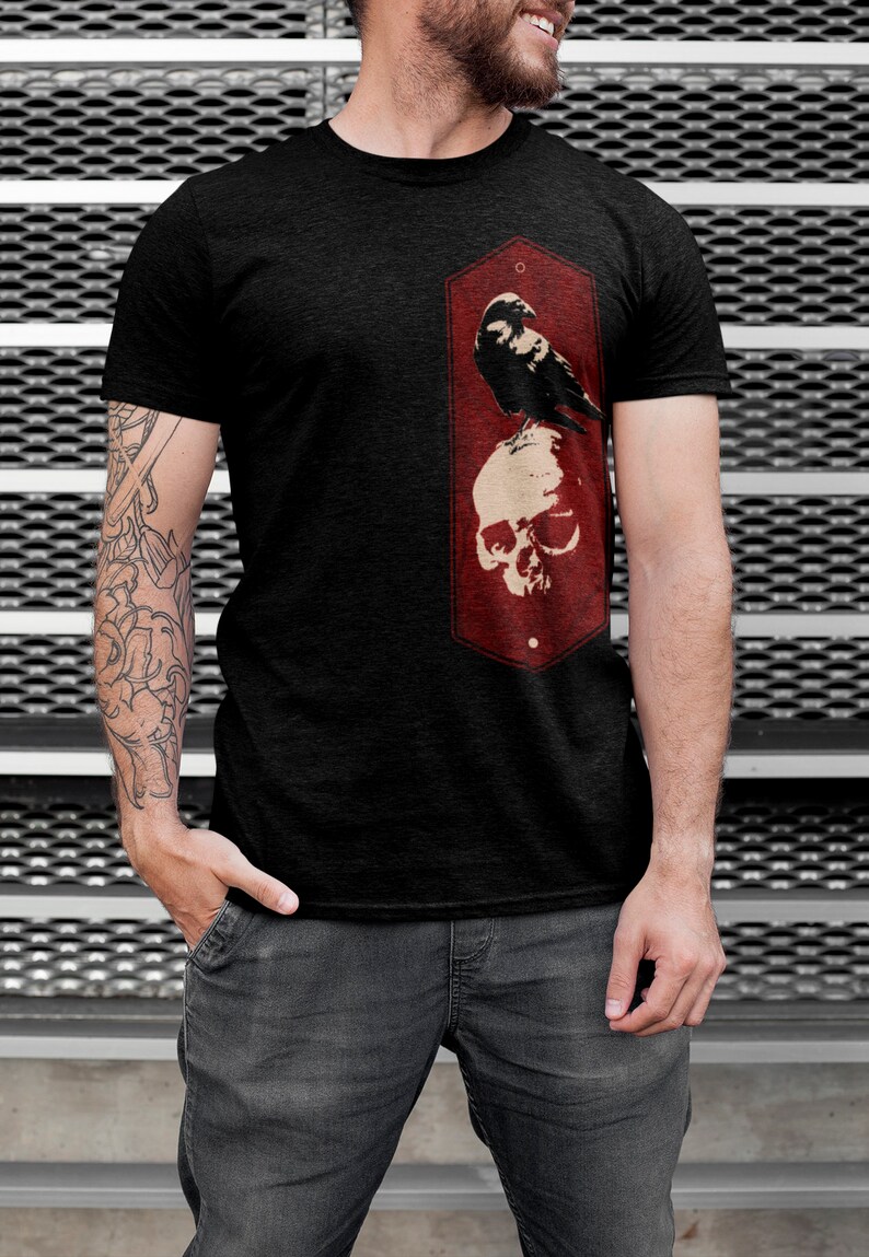 May include: A black t-shirt with a red graphic of a crow perched on a skull. The graphic is in a vintage style with a distressed look.