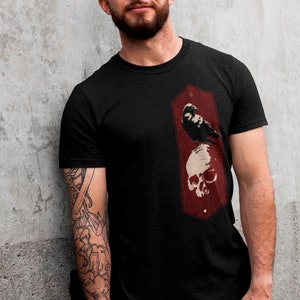 May include: Black t-shirt with a red graphic of a crow perched on a skull.
