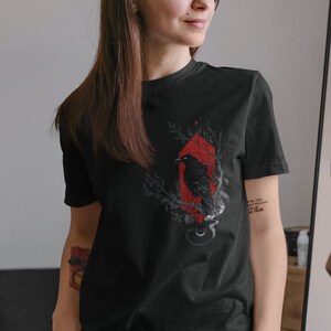 May include: Black t-shirt with a graphic of a black raven perched on a branch with red accents. The text "I tell you, never fear the shadows, for they hold no fear" is printed on the shirt.