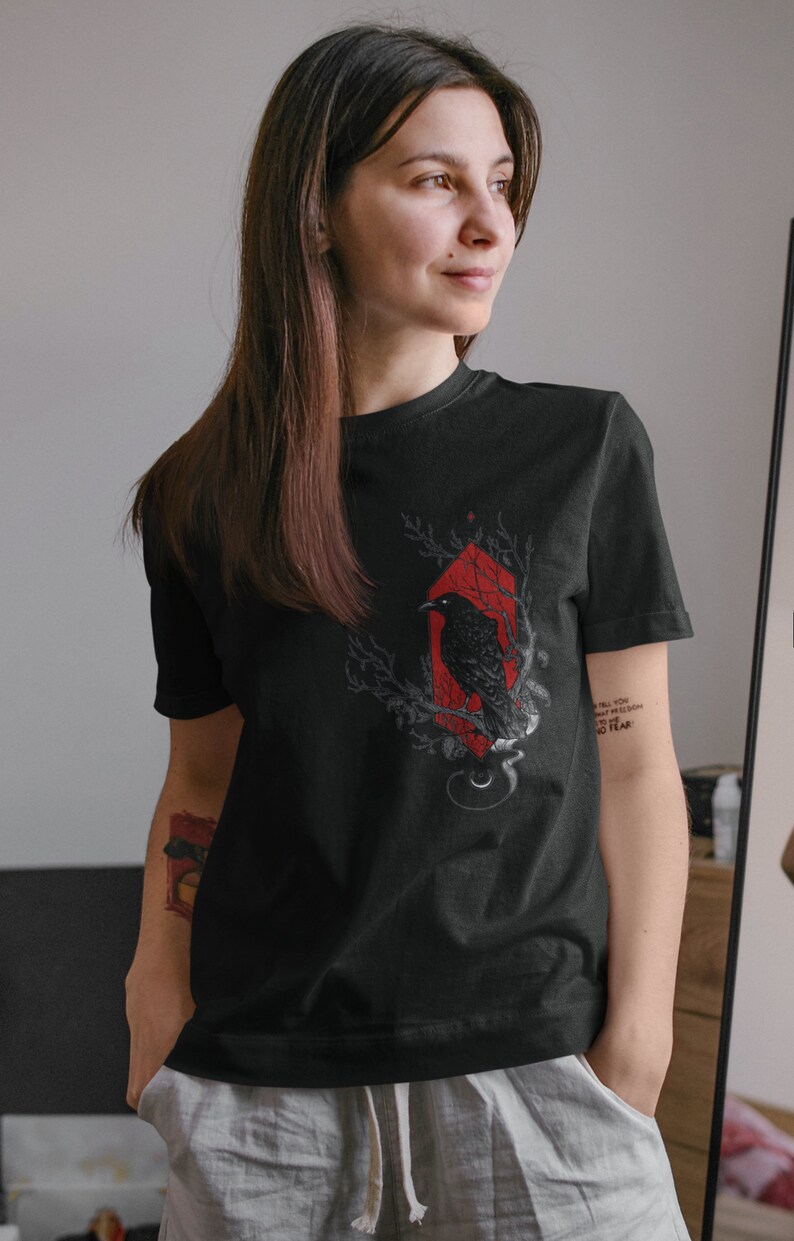 May include: Black t-shirt with a graphic of a black raven perched on a branch with red accents. The text "I tell you, never fear the shadows, for they hold no fear" is printed on the shirt.
