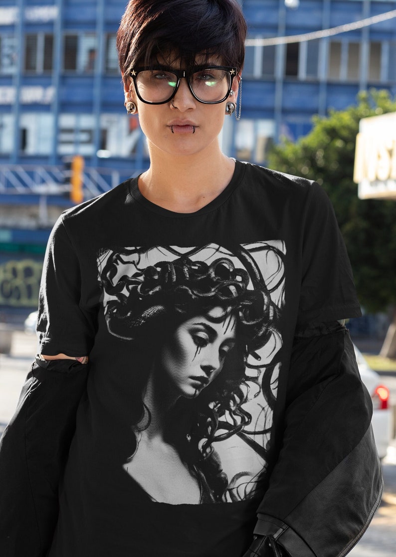 May include: Black t-shirt with a graphic print of a woman with snakes in her hair. The woman is looking down and has a sad expression on her face.