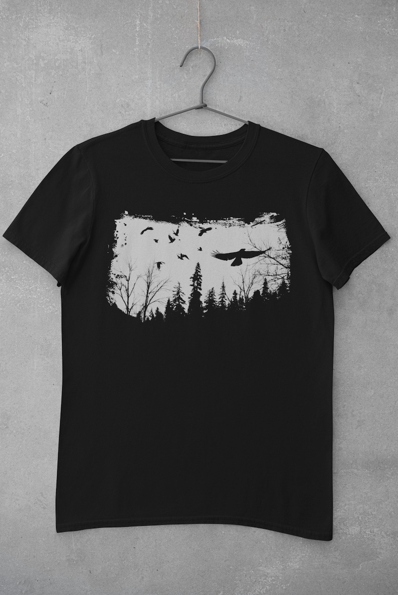 May include: Black t-shirt with a white graphic print of a forest silhouette with birds flying over it.