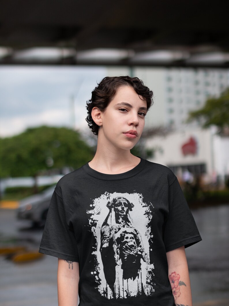 May include: A black t-shirt with a white graphic print of a woman in a hooded robe with a skull on her chest. The graphic has a distressed, vintage look.