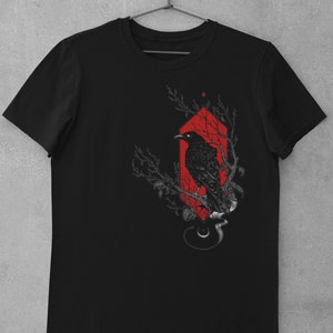 May include: Black t-shirt with a graphic of a crow perched on a branch inside a red geometric shape.