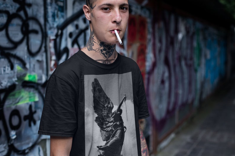 May include: A black t-shirt with a graphic print of a winged statue. The statue is in a black and white color scheme and appears to be holding a rope.