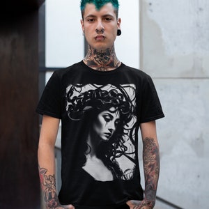 May include: A black t-shirt with a graphic print of a woman with snakes in her hair. The woman is looking down and has a sad expression on her face. The graphic is in black and white.