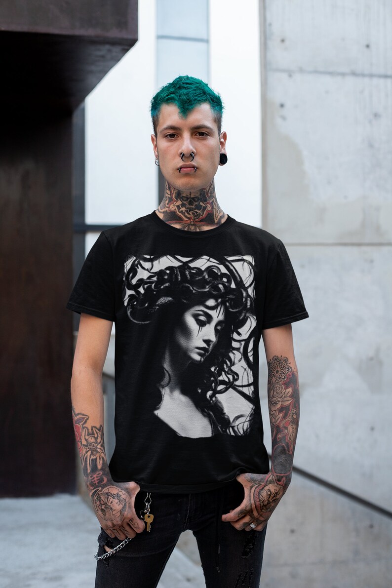 May include: A black t-shirt with a graphic print of a woman with snakes in her hair. The woman is looking down and has a sad expression on her face. The graphic is in black and white.