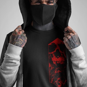 K&ouml;nnte beinhalten: Schwarzes T-Shirt mit einem roten Totenkopf-Motiv. Der Totenkopf ist stilisiert und hat ein gezacktes, geometrisches Design.