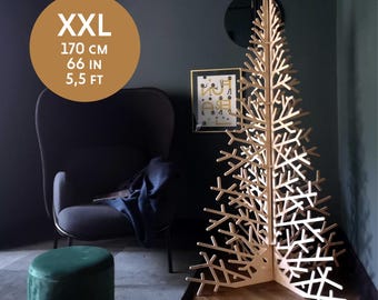 May include: A large wooden Christmas tree with a natural finish. The tree is 66 inches tall and stands on a wooden floor. The tree is in a room with a gray wall and a green velvet ottoman.