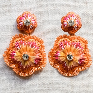 May include: A pair of orange and pink flower-shaped earrings with a clear rhinestone in the center of each flower.