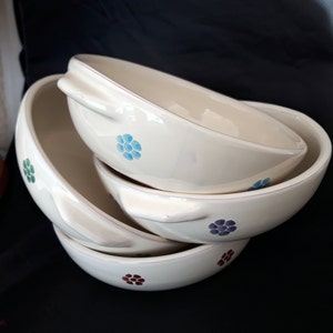 May include: Three white ceramic bowls with floral designs in blue, green, purple, and brown. The bowls are stacked on top of each other.