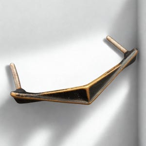 May include: A geometric cabinet pull with a black and gold finish. The handle has a V-shape design with two threaded posts for mounting. The hardware is made of metal and is suitable for drawers or cabinet doors.