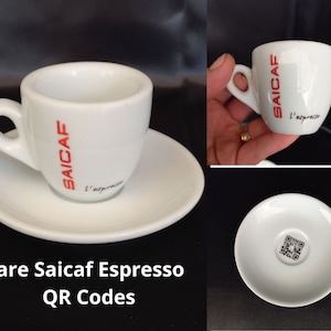 Op de afbeelding: Witte espresso kop en schotel set. De kop heeft een handvat en het woord "SAICAF" in rood, met "L'espresso" eronder. De schotel heeft een QR-code. De set is ontworpen voor espresso koffie.