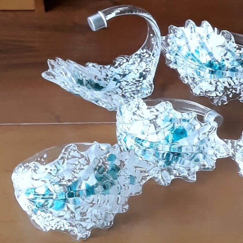 K&ouml;nnte beinhalten: Ein Set aus transparenten Glasservierschalen mit einem einzigartigen, wellenartigen Design. Die Schalen haben ein strukturiertes, mattiertes Aussehen mit t&uuml;rkisfarbenen Akzenten. Jede Schale hat einen gebogenen Griff. Das Set wird auf einer Holzoberfl&auml;che pr&auml;sentiert.