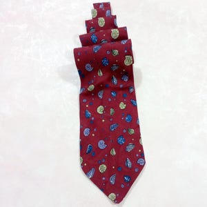 May include: A burgundy tie with a repeating pattern of blue, green, and purple seashell designs. The tie is rolled up, showcasing the pattern and the fabric's texture. The tie is a classic accessory.