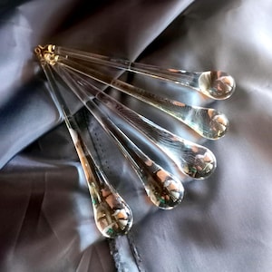 May include: A set of five clear, teardrop-shaped glass chandelier crystals arranged in a fan pattern. Each piece features a long, slender, tapered body ending in a rounded, bulbous tip, with a small metal loop at the top for hanging purposes.