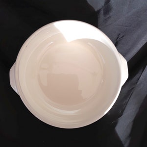 May include: White ceramic baking dish with two handles. The dish is round and has a smooth, glossy finish.