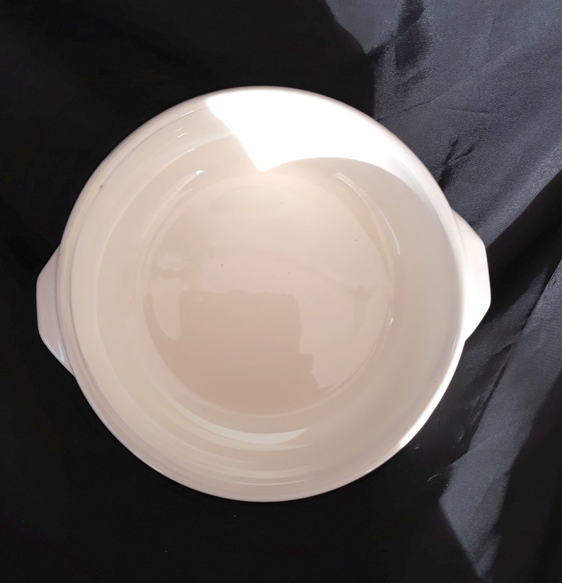 May include: White ceramic baking dish with two handles. The dish is round and has a smooth, glossy finish.
