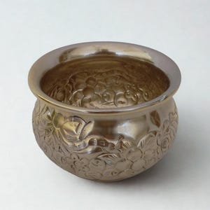 以下が含まれることがあります： エンボス加工された花の模様が施された、メタリックゴールド色のボウル。ボウルは丸みを帯びた形状で、広い縁があります。外側には、花と葉の精巧なレリーフ彫刻が施されています。