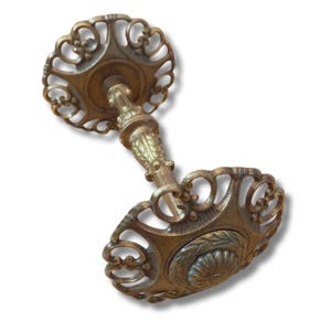 以下が含まれることがあります： 精巧なアンティーク真鍮のドアノブ。繊細な透かし彫りと花のディテールが特徴です。装飾的なステムで接続された2つの円形プレートがあります。真鍮は暖かく、古びた風合いで、ヴィンテージの職人技を思わせます。クラシックなハードウェアです。