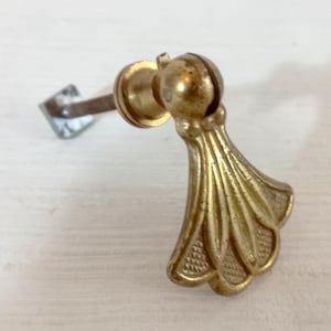 Op de afbeelding: Close-up van een vintage messing ladeknop. De knop heeft een decoratief, waaiervormig ontwerp met ingewikkelde details. De hardware omvat een metalen staaf en een montageplaat.