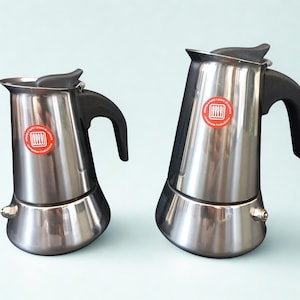 Op de afbeelding: Een witte keramische mok met een zwarte handgreep en de tekst "But First, Coffee" in een vetgedrukte, zwarte letter. De mok staat tegen een vage achtergrond, wat het eenvoudige ontwerp benadrukt.