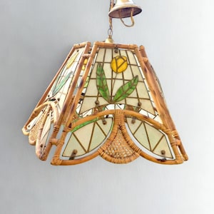 May include: A vintage hanging lamp with a bamboo frame and stained glass panels. The panels feature yellow flower and green leaf designs. The lamp has a bell-shaped top and a woven rattan base, creating a warm, inviting aesthetic.