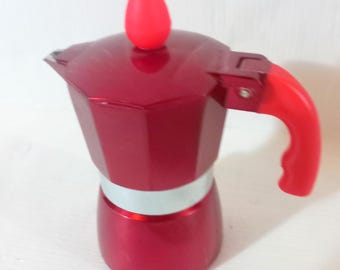 May include: A red stovetop espresso maker with a red handle and top knob. The coffee pot has a silver band around the middle and a shiny finish. The espresso maker is designed to brew coffee on a stovetop.