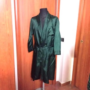 May include: A dark green satin robe with a shawl collar and a matching belt. The robe has long sleeves and a pocket on the front. The robe is displayed on a black mannequin.
