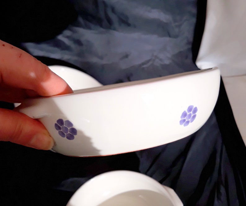 May include: Two white ceramic bowls with a blue floral design. The bowls are slightly curved and have a lip around the edge.