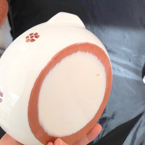 May include: White ceramic bowl with a terracotta rim and a floral design. The bowl is hand-painted with small red flowers.