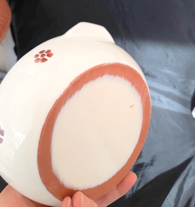 May include: White ceramic bowl with a terracotta rim and a floral design. The bowl is hand-painted with small red flowers.
