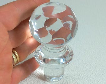 May include: A clear glass bottle stopper with a faceted ball top. The stopper is designed to fit a standard bottle.